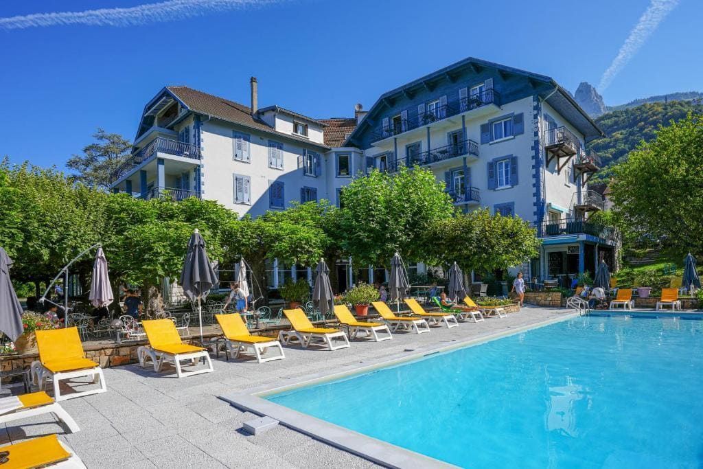 Piscine de complexe hôtelier avec chaises longues jaunes, palmiers et un grand bâtiment d'hôtel sous un ciel bleu