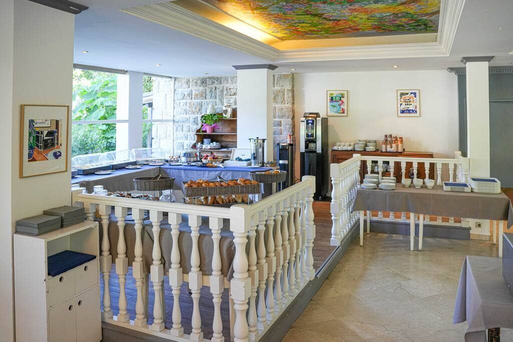 Salle à manger lumineuse avec balustrade blanche, nappes bleues, grandes fenêtres et plafond peint