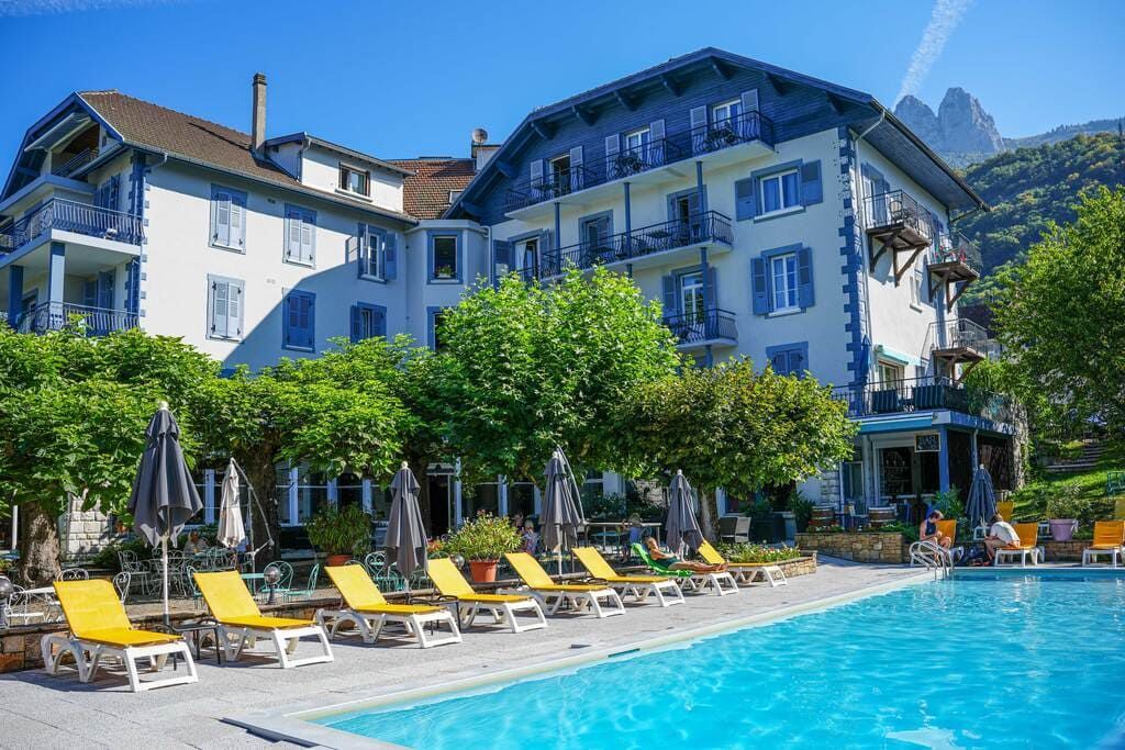 Piscine d'hôtel avec chaises longues jaunes, arbres et un bâtiment blanc sous un ciel bleu