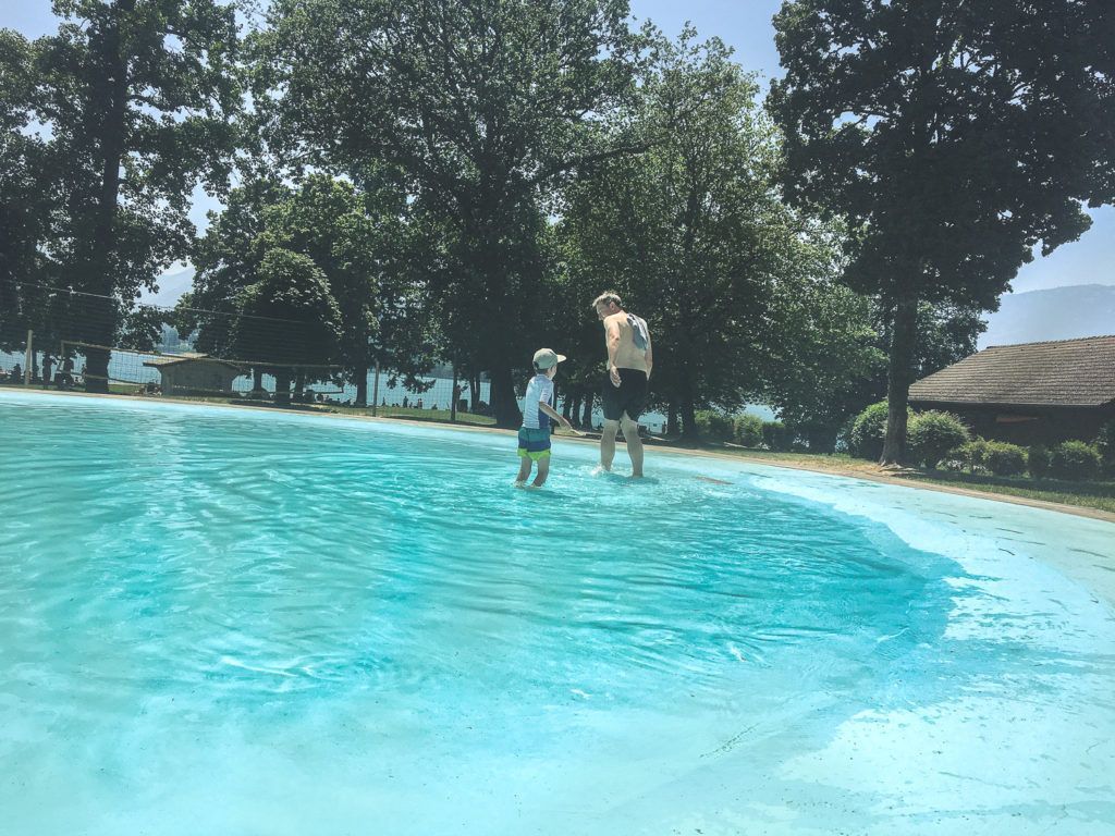 Des gens pataugent dans une piscine d'un bleu éclatant, près d'arbres et d'une hutte au toit de chaume.