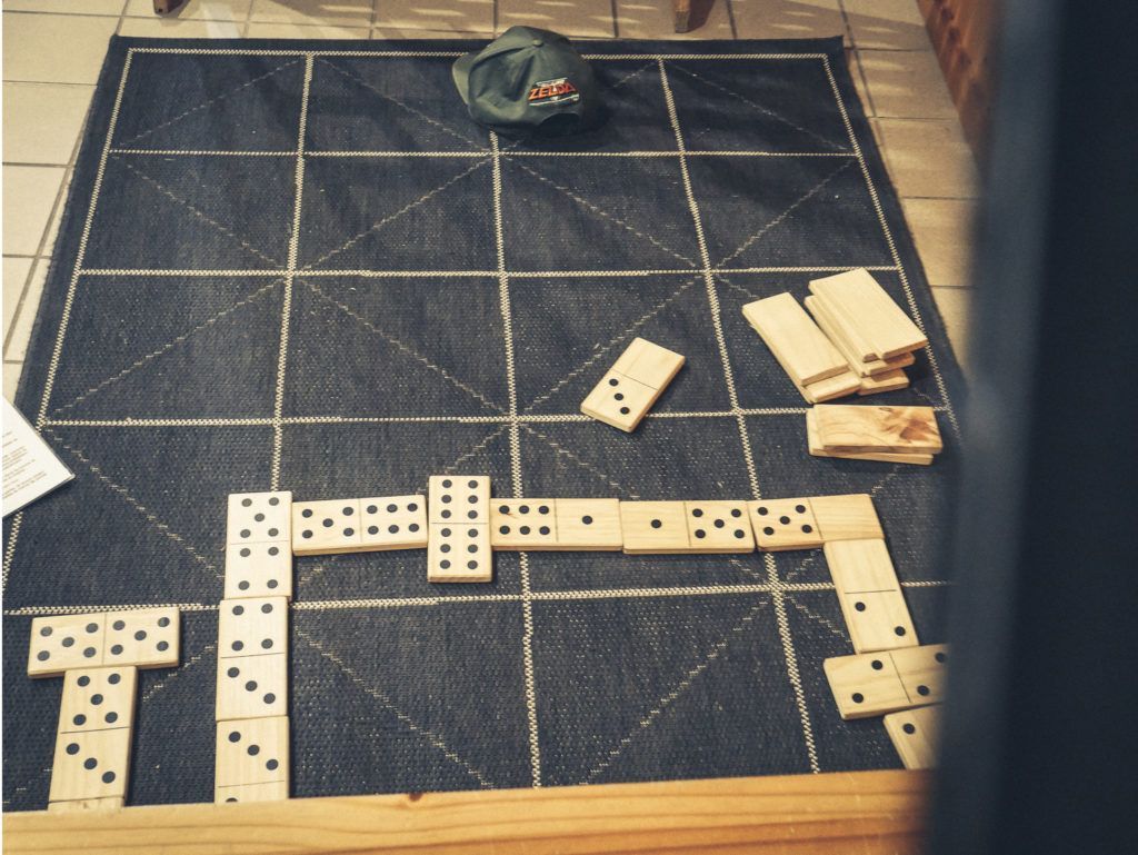 Des dominos disposés en ligne sur un tapis sombre, avec une pile de tuiles et un petit bol à proximité.