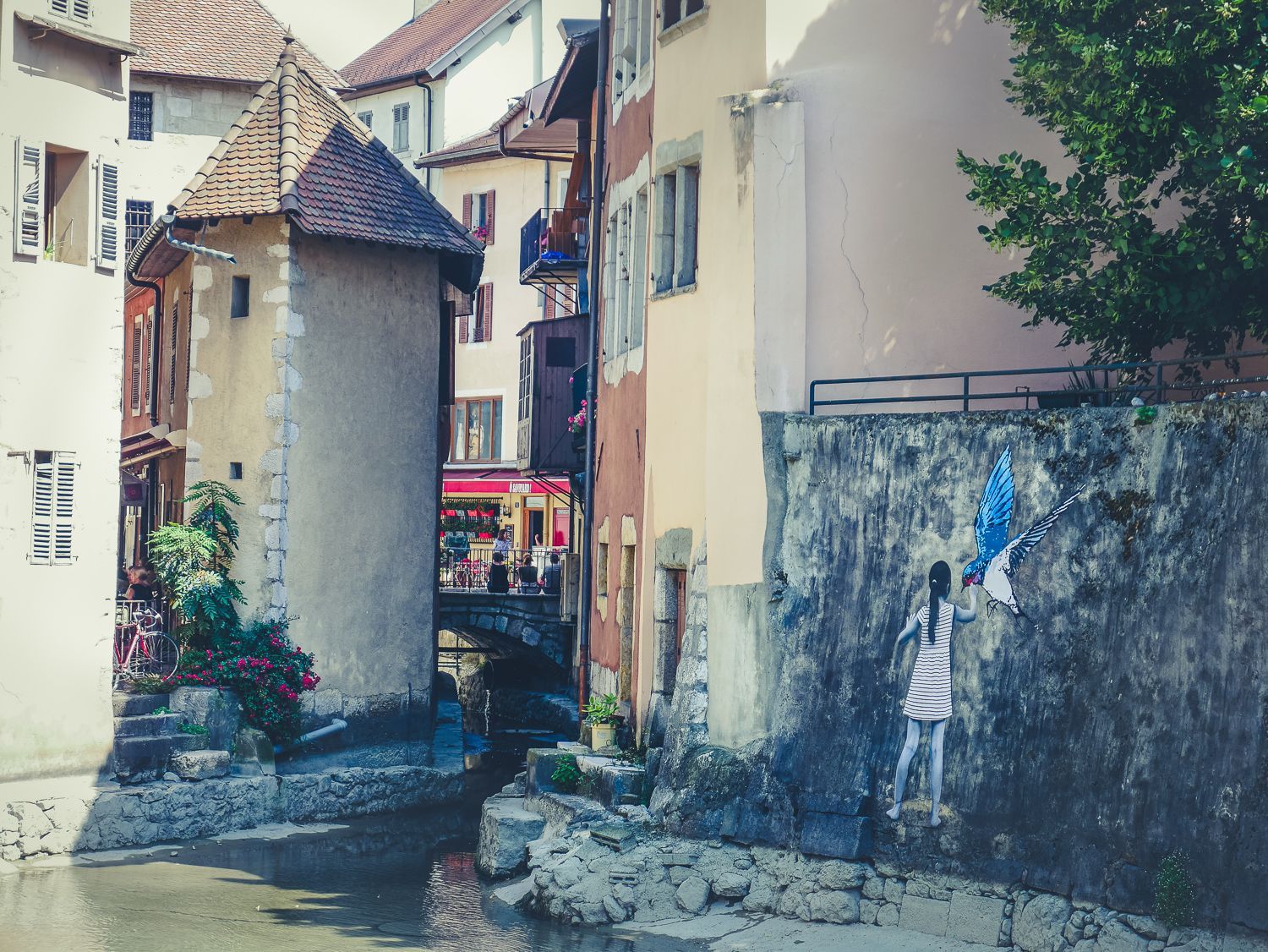 Rue européenne étroite bordée de bâtiments aux teintes pastel, de murs en pierre et d'une enseigne suspendue au bord d'un canal.