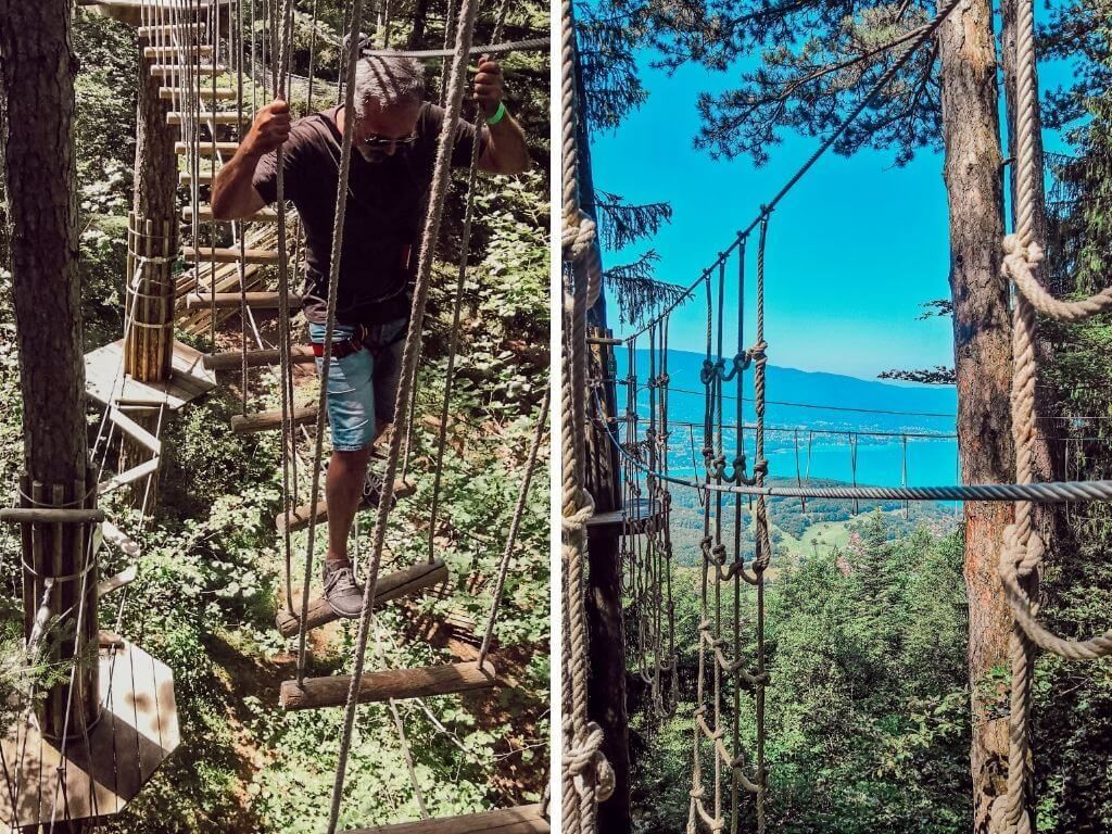 Une personne traverse un pont de corde dans une forêt boisée, avec un ciel bleu et de l'eau au loin.