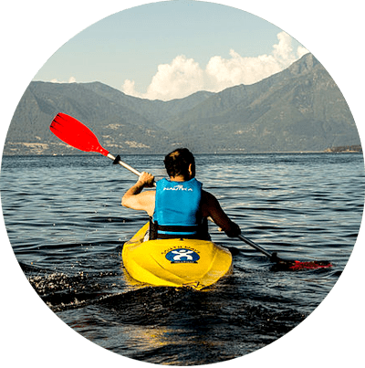 Un kayakiste pagaye dans un kayak jaune sur une eau calme, avec des montagnes en arrière-plan.