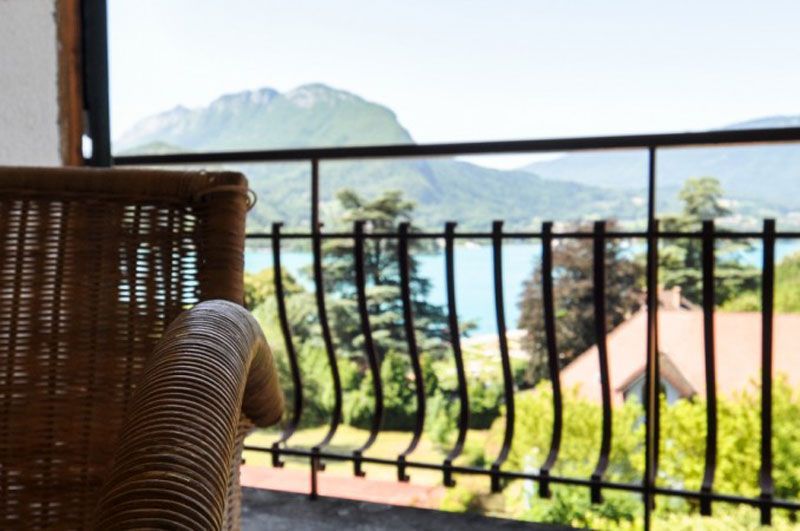 Fauteuil en osier sur un balcon donnant sur la mer, les montagnes et les toits, au-delà d'une balustrade.