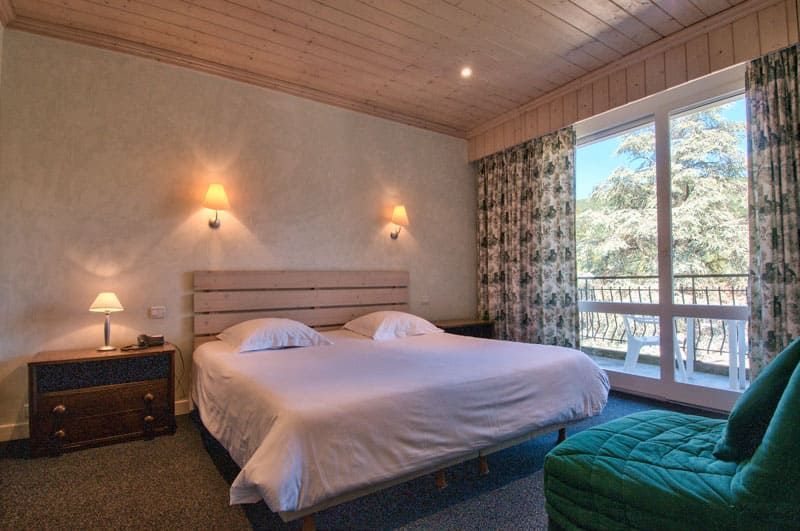Chambre confortable avec un grand lit, des lampes de chevet, un fauteuil turquoise et des portes coulissantes donnant sur un balcon.