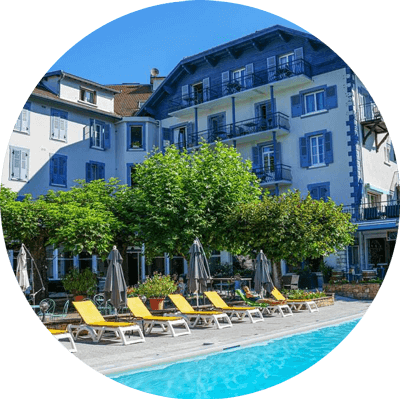 Piscine d'hôtel avec chaises longues jaunes, arbres verts et un bâtiment bleu et blanc sous un ciel lumineux