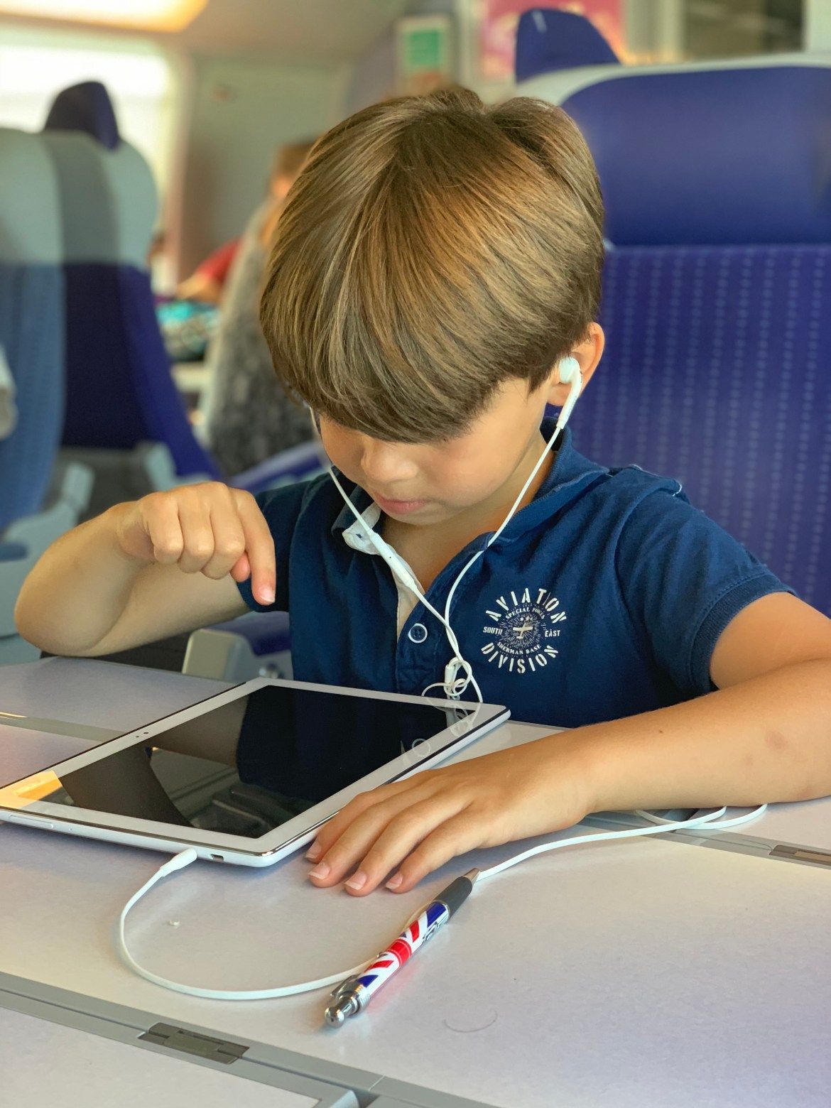 Enfant utilisant une tablette sur un siège d'avion, portant des écouteurs et regardant l'écran.
