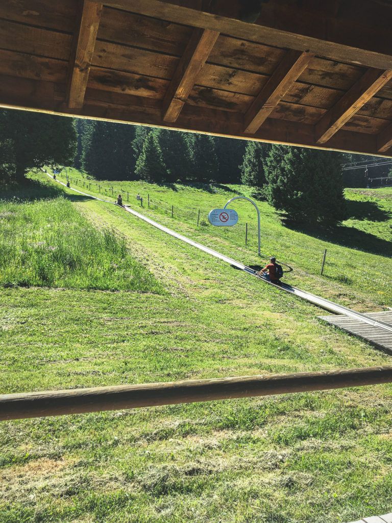 Piste de ski herbeuse avec un toit en bois au-dessus et une personne assise près du bas, au bord de la piste.