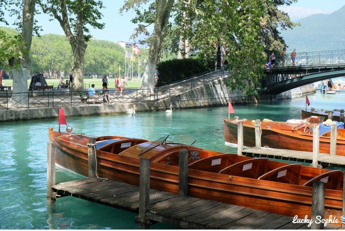 Des barques en bois amarrées sur un canal turquoise, près des arbres et d'un petit pont
