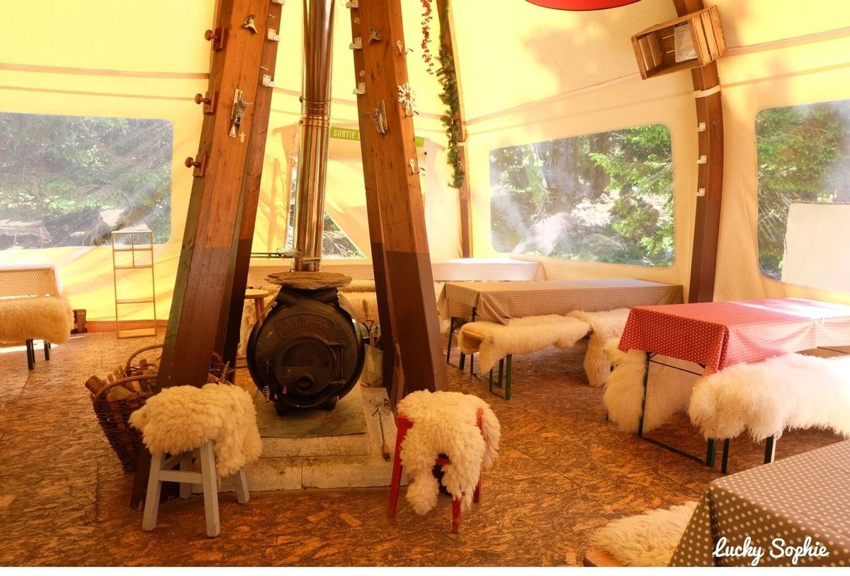 Intérieur de yourte confortable avec un poêle central, des tabourets en fourrure et des lits sous un éclairage chaleureux et de grandes fenêtres