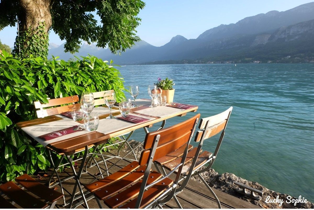 Table et chaises de café au bord du lac, près de l'eau bleue, avec les montagnes en arrière-plan.