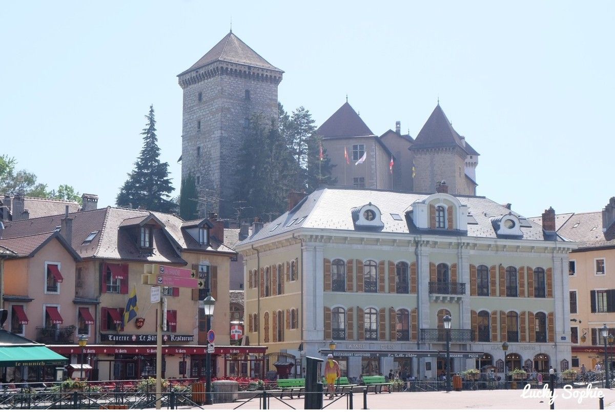 Place historique de la ville avec des bâtiments colorés et une tour de château en pierre en arrière-plan, sous un ciel dégagé