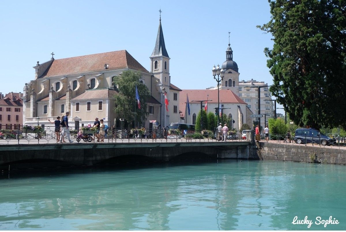 Bord de canal avec bâtiments historiques, pont, clocher d'église et bateaux sous un ciel bleu clair