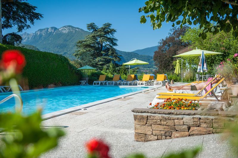 Piscine ensoleillée d'un complexe hôtelier avec chaises longues, parasols et vue sur la montagne