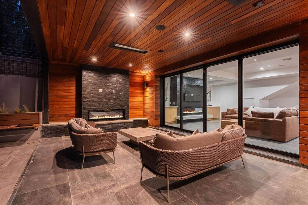 Modern lounge with leather seating, stone fireplace, wood ceiling, and glass doors to an adjacent room