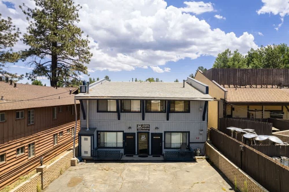 Courtyard view of a gray two-story apartment building with balconies under a sunny sky