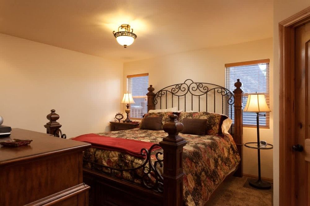 Cozy bedroom with wrought-iron bed, patterned bedding, two lamps, and warm beige walls
