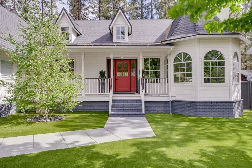 White house with red front door, front porch, and curved windows amid a green lawn