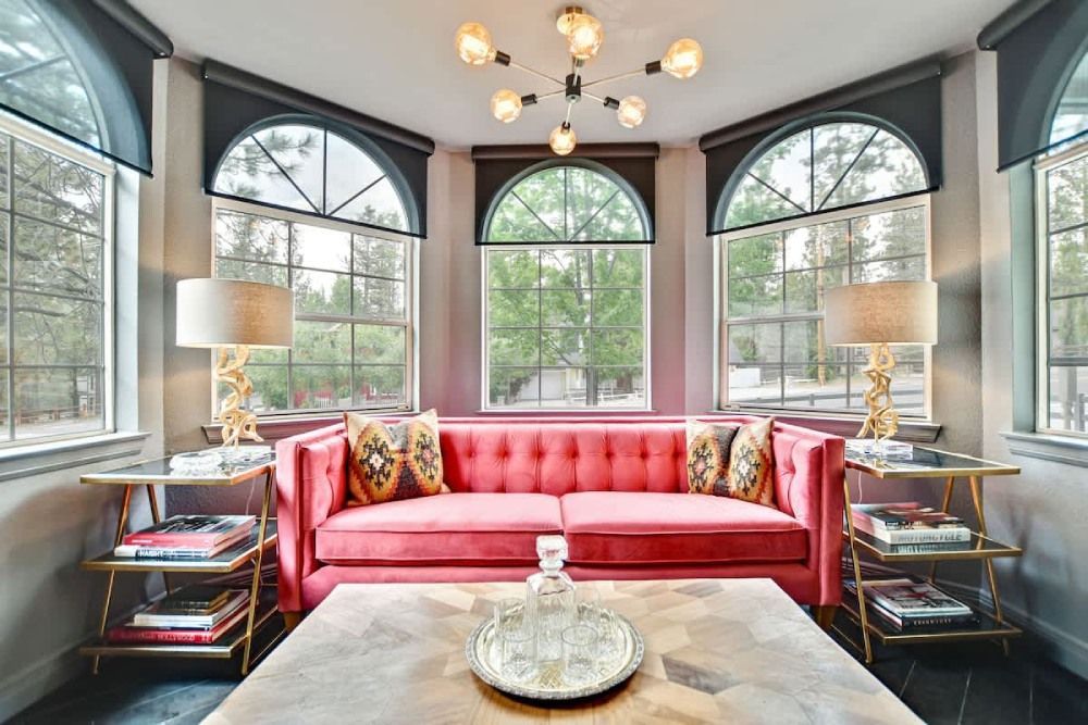 Bright living room with a pink sofa, large arched windows, and a marble coffee table