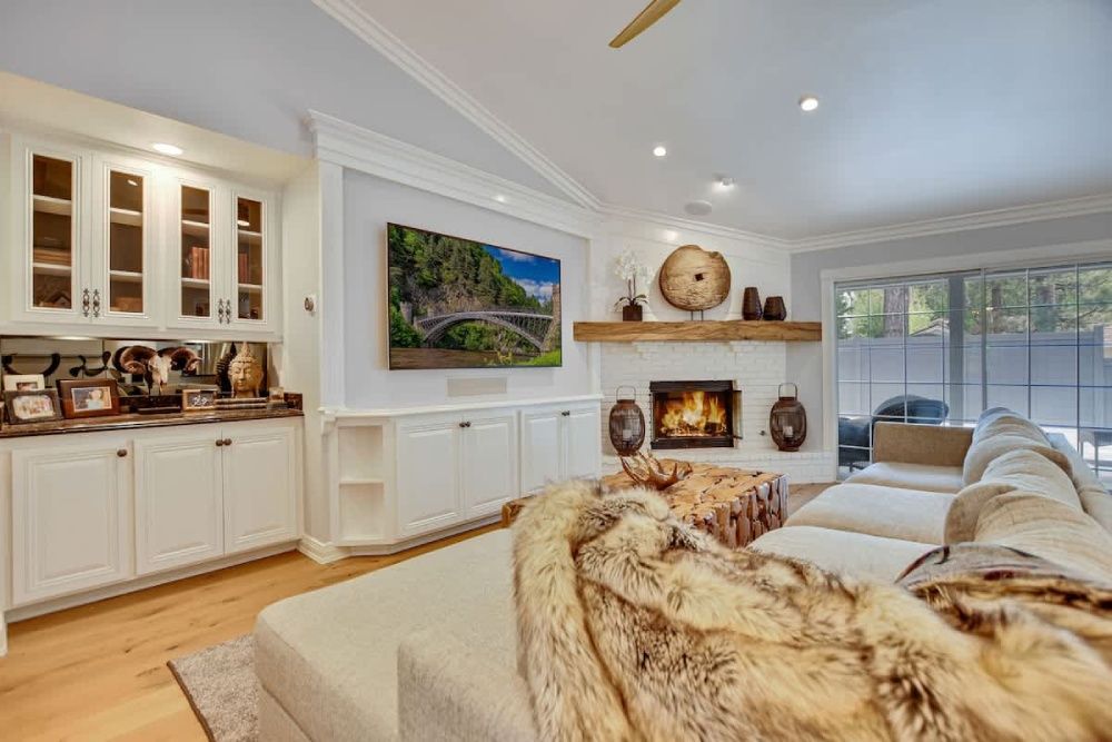 Bright living room with white built-ins, fireplace, wall TV, beige sofa, and large sliding glass doors