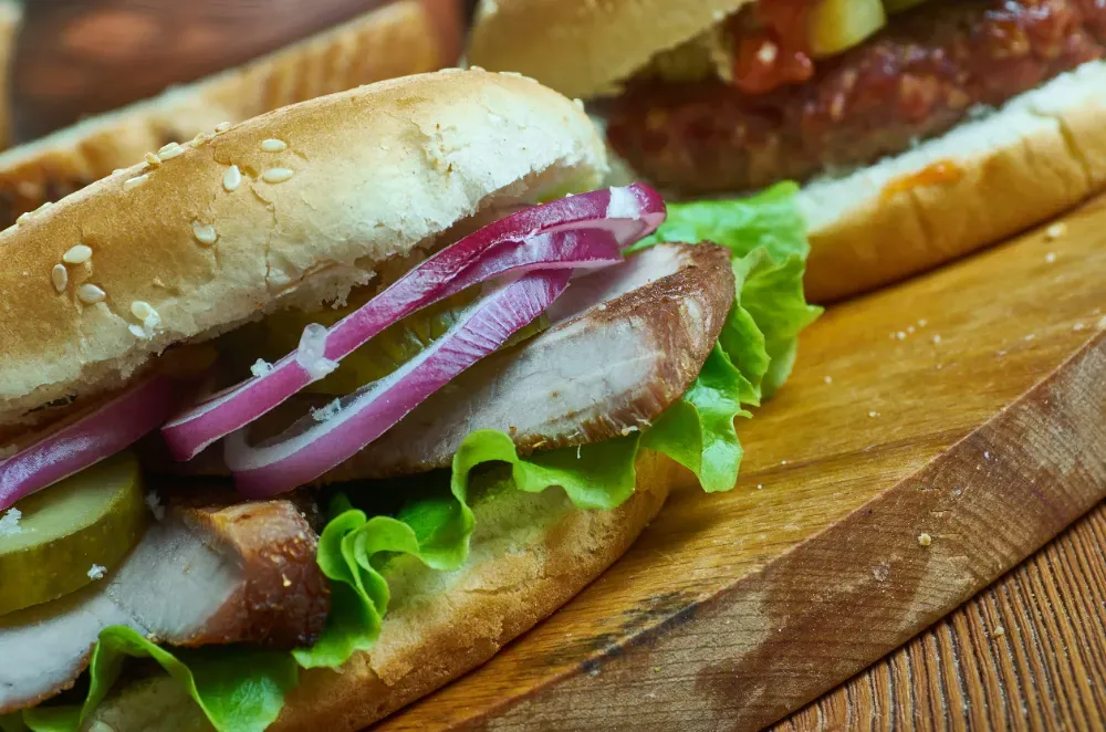 Dos sándwiches gourmet con carne, cebolla roja y lechuga en panecillos tostados con semillas de sésamo