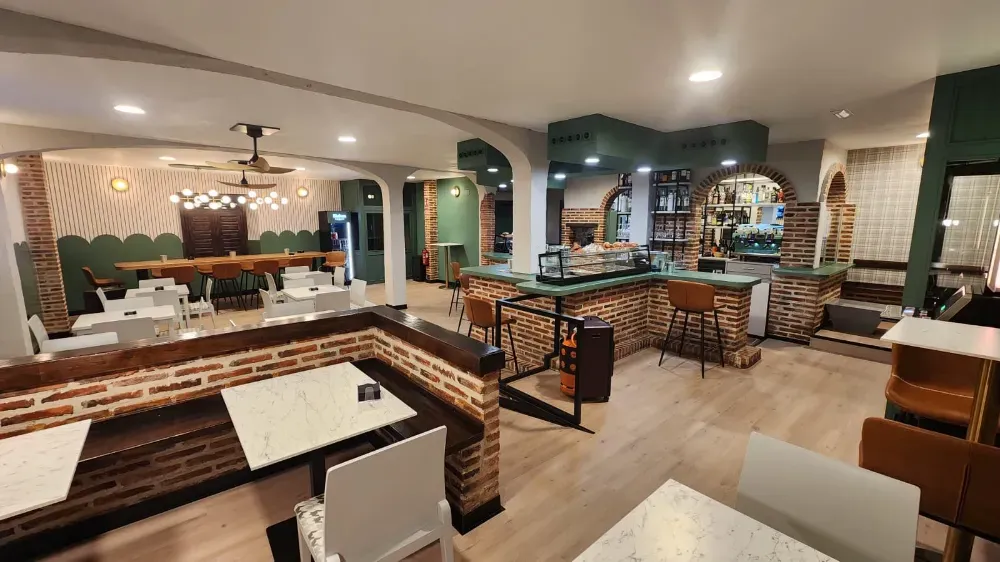 El interior de un restaurante moderno cuenta con detalles de paredes de ladrillo visto, mesas blancas, paredes verdes 