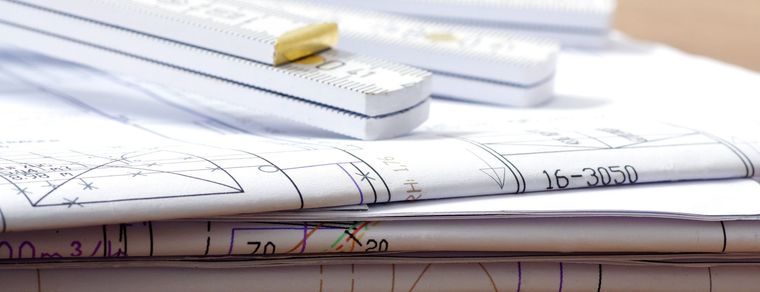 Plans architecturaux roulés et empilés, avec un crayon sur le dessus.