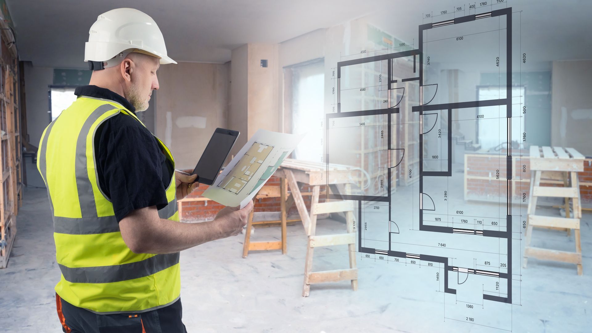 Ouvrier du bâtiment portant un casque et un gilet de sécurité examinant des plans sur un chantier de rénovation de maison