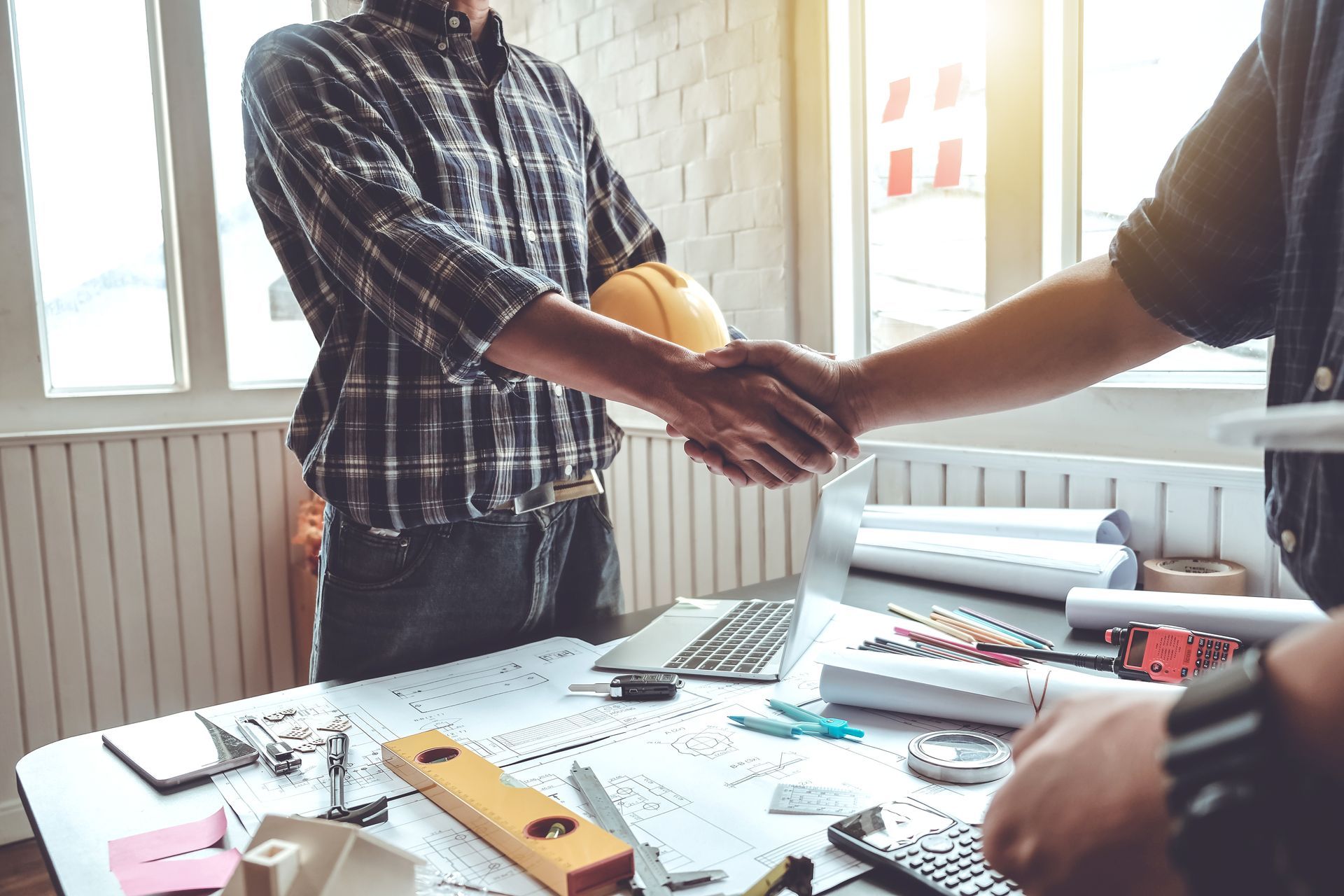 Deux personnes se serrent la main par-dessus une table de bureau encombrée, près d'une fenêtre.