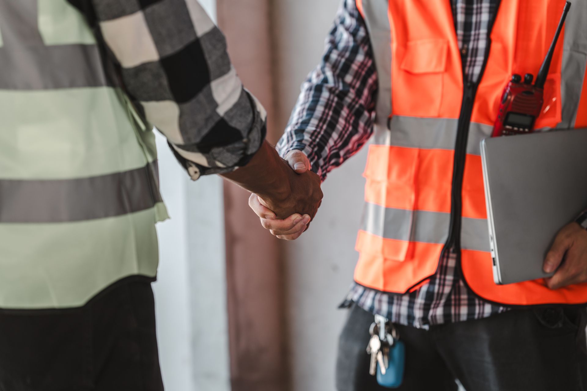 Deux ouvriers portant des gilets de sécurité se serrent la main sur un chantier de construction tout en tenant un bloc-notes.