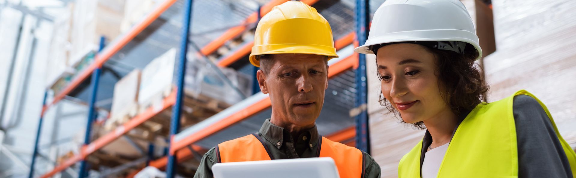 Deux ouvriers portant des casques de chantier examinent une tablette dans une allée d'entrepôt.