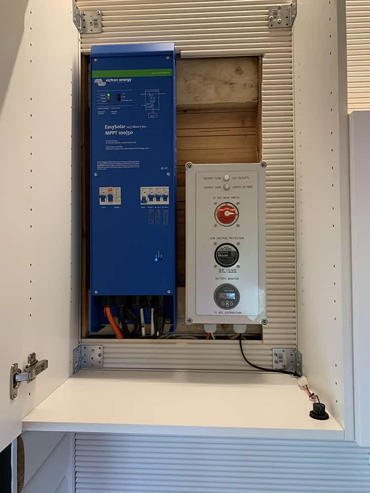 A blue solar energy inverter and a white control panel are mounted in a cabinet. The cabinet door is open, and wiring is visible.
