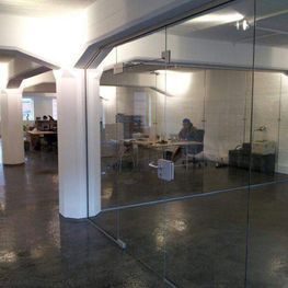 Ein Raum mit vielen Glaswänden und einer Person, die an einem Schreibtisch sitzt.