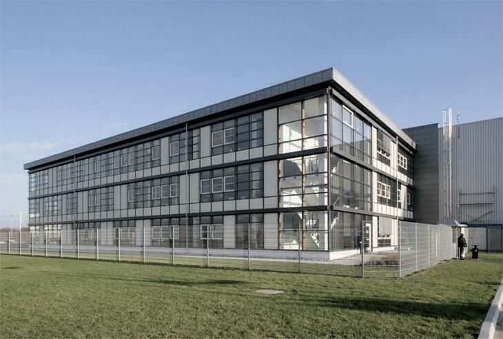 Ein großes Gebäude mit vielen Fenstern ist von Gras und einem Zaun umgeben.