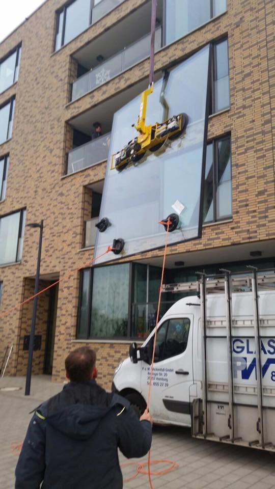 Ein Mann steht vor einem Lieferwagen und hebt ein großes Glasfenster an.