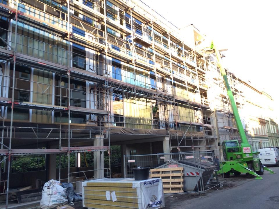 Mit Gerüsten und einem grünen Kran wird ein großes Gebäude errichtet.