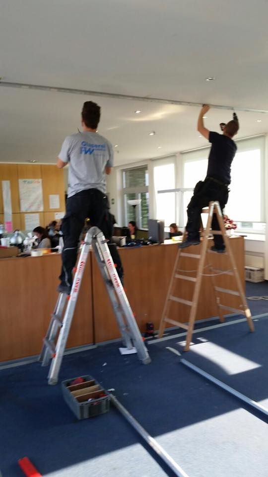 Zwei Männer arbeiten an einer Decke und einer steht auf einer Leiter