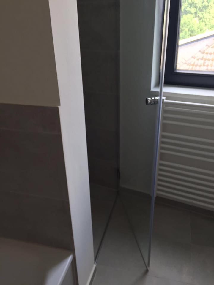 Ein Badezimmer mit einer Glasduschtür und einem Fenster.