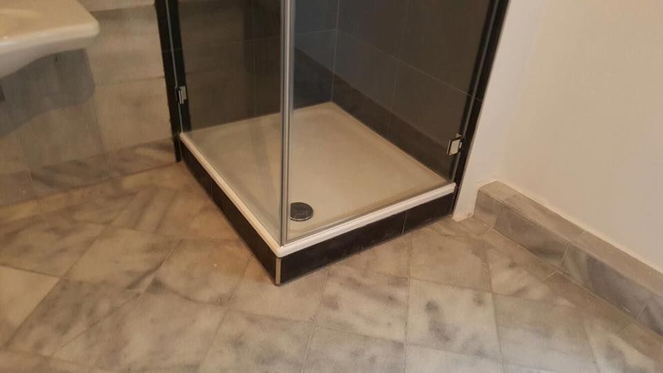 In einem Badezimmer steht eine Duschkabine auf einem gefliesten Boden.