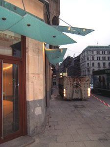 Auf dem Bürgersteig vor einem Gebäude steht ein Müllcontainer.