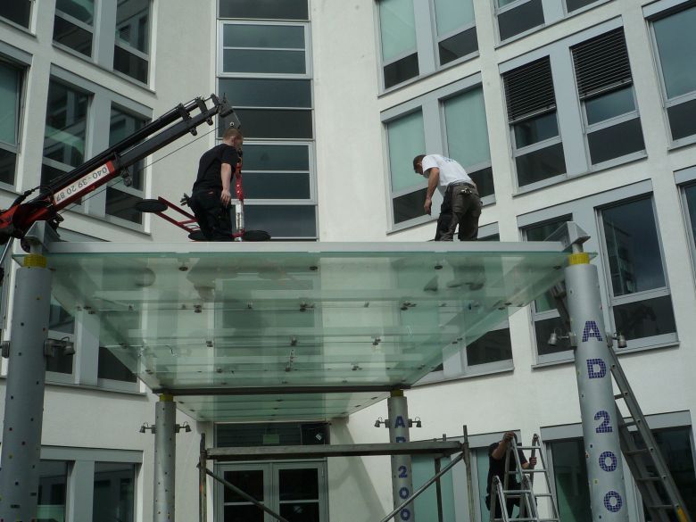 Zwei Männer arbeiten an einem Glasdach außerhalb eines Gebäudes