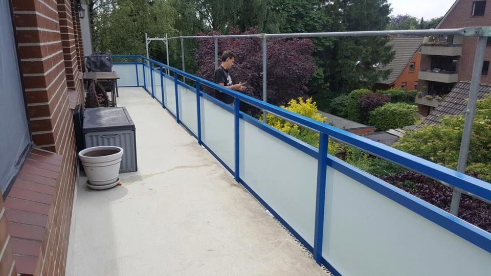 Ein Mann steht auf einem Balkon mit blauem Geländer.