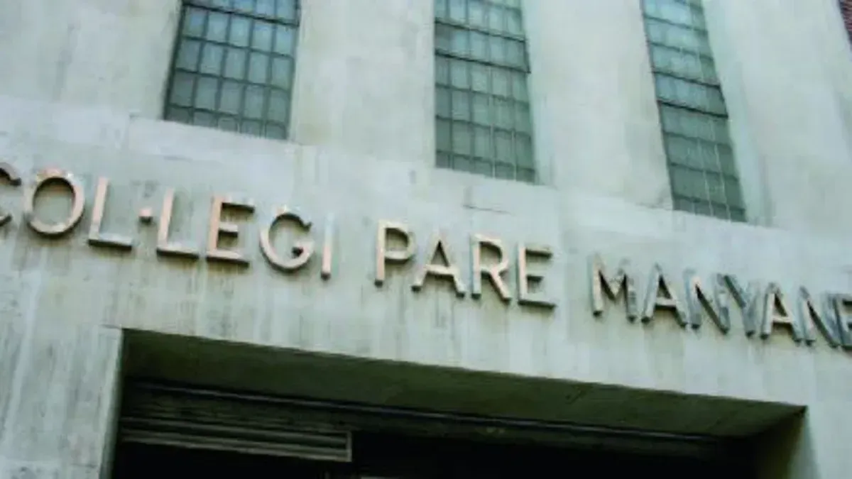 Building facade with gold lettering reading “COLLEGI PARE MUMAN” above an entrance