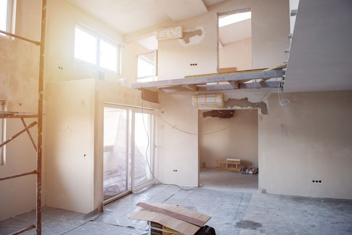 Interior de un edificio en construcción: habitaciones llenas de luz, andamios, paredes expuestas y escombros en el suelo.