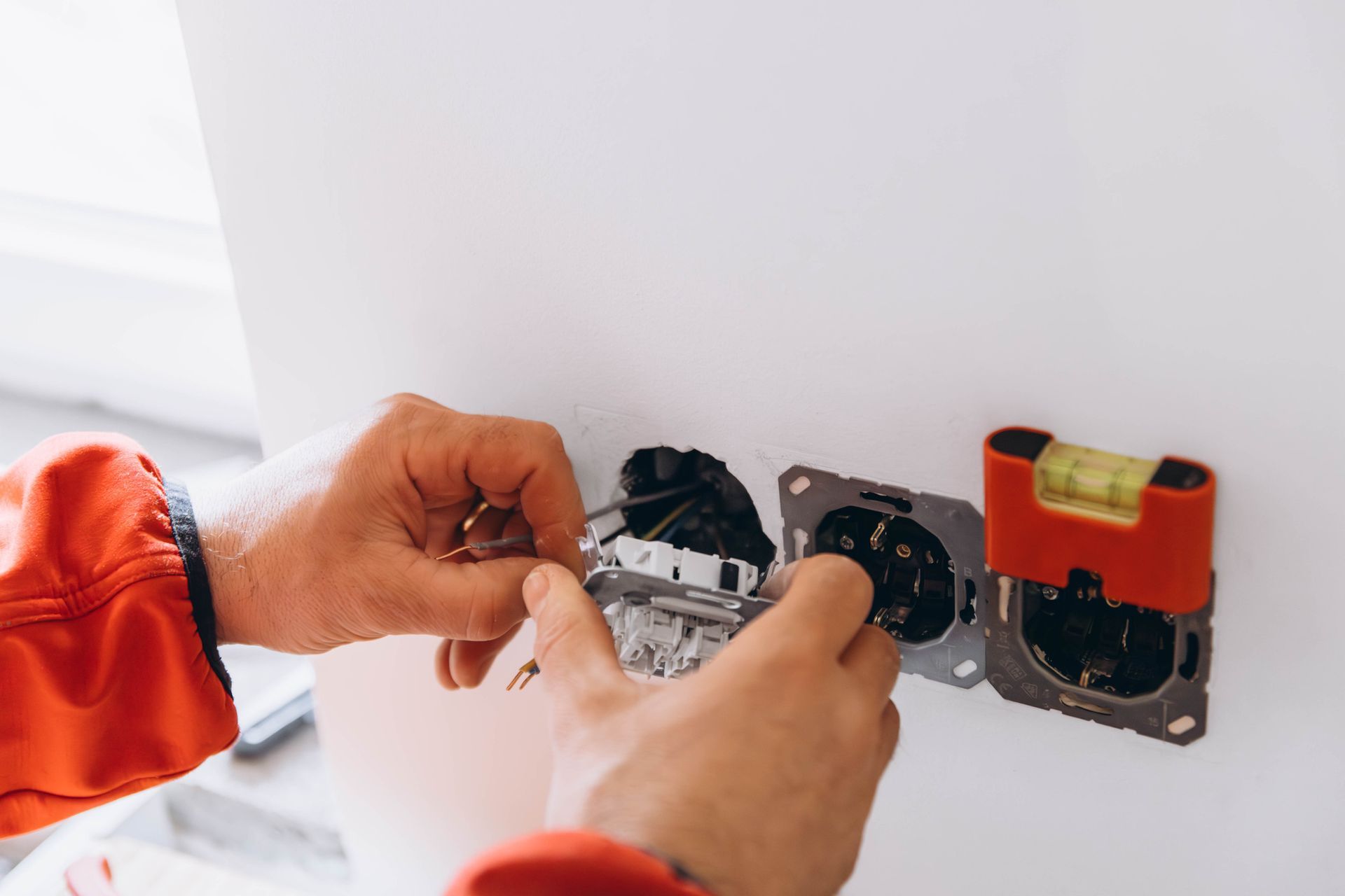 Persona con chaqueta roja instalando un tomacorriente eléctrico en una pared blanca.