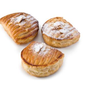 Três pastéis com açúcar de confeiteiro por cima em uma superfície branca