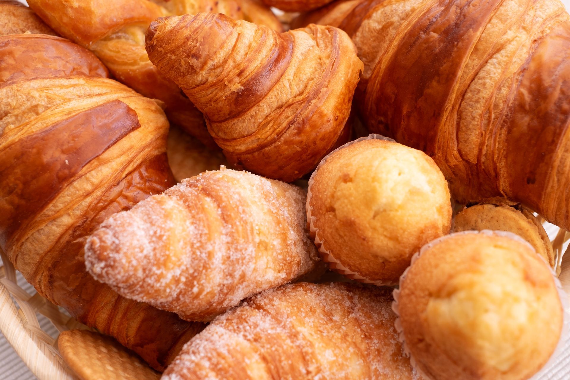 Uma cesta cheia de croissants e muffins sobre uma mesa.
