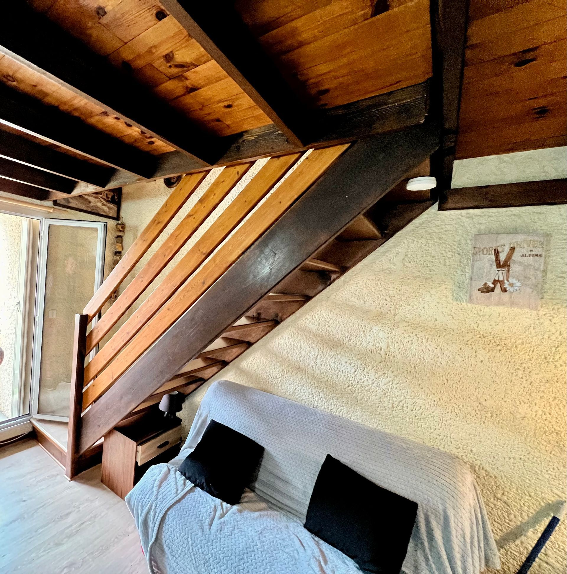 Chambre mansardée avec escalier en bois apparent, canapé bas et plafond en bois incliné sous l'escalier.