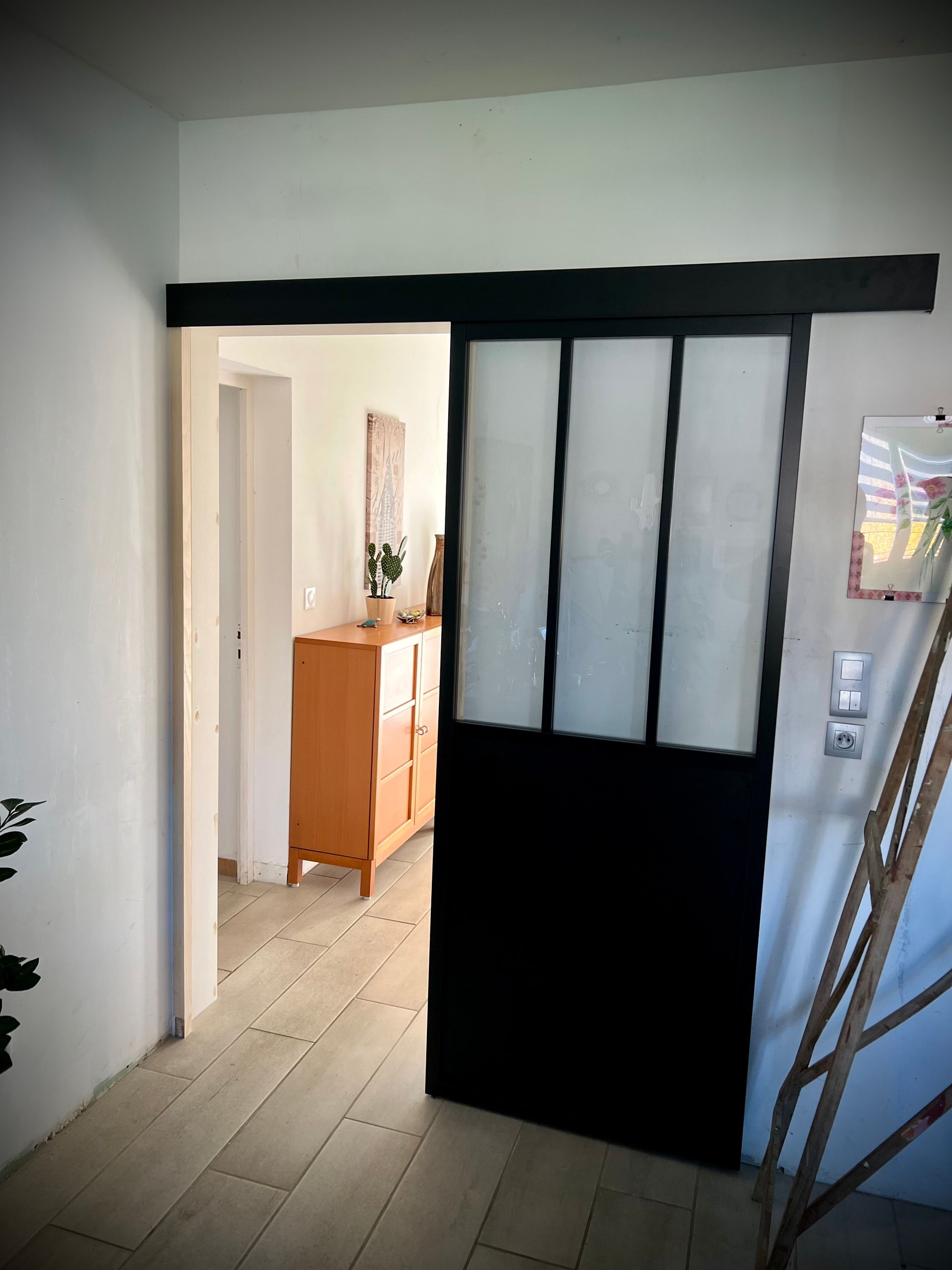 Couloir intérieur avec une porte à cadre noir et des panneaux coulissants en verre dépoli.